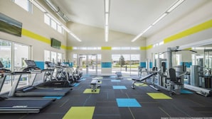 Ein Fitnessstudio mit Laufbändern, Kraftgeräten und einem großen Fenster mit Blick ins Freie.