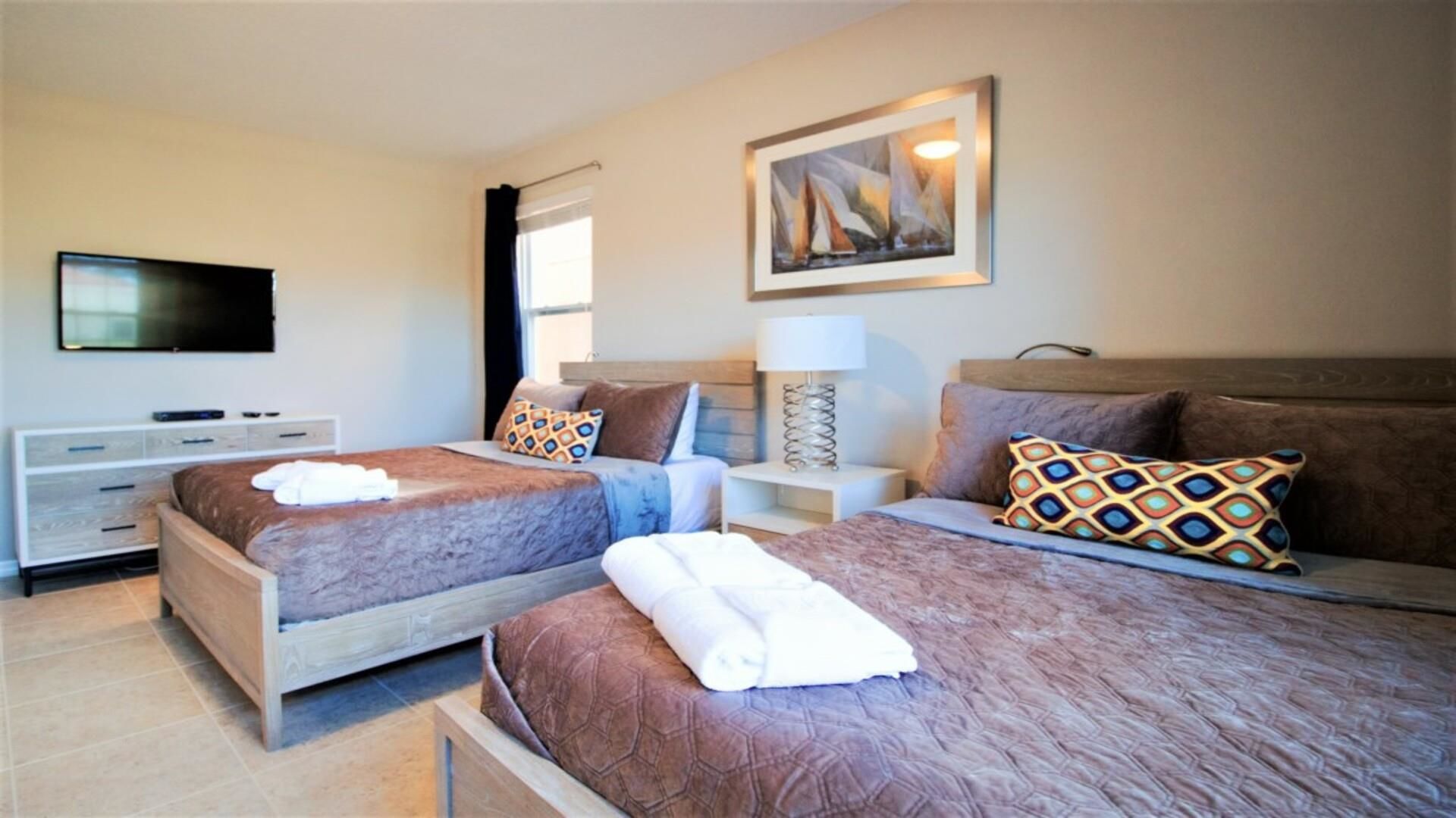 A hotel room with two beds, a TV, a painting, and a lamp.