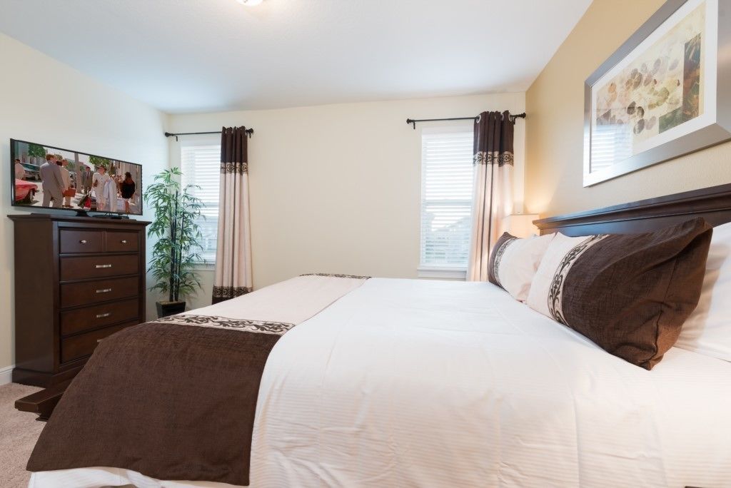 A bedroom with a large bed, a dresser, a television on a stand, and a window with curtains.
