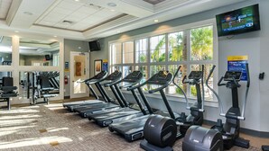 Ein Fitnessraum mit Laufbändern, Ergometer und einem Fernseher, der ein Sportereignis zeigt.