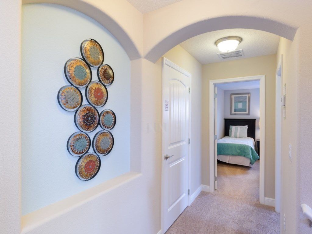 A hallway with a decorative wall art installation, a door, and a bedroom with a bed and a nightstand.