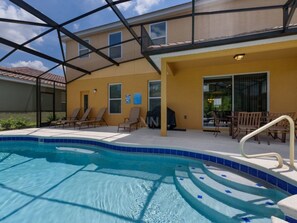 Una piscina con cerramiento de vidrio, camastros y un área de patio techada.