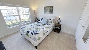 A bedroom with a large window, a bed with floral bedding, two bedside tables with lamps, and a wall-mounted artwork. - Aco256584 - Storey Lake Resort - 4 Bed 3 Baths Townhome (Kissimmee)