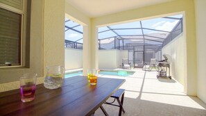 A sunlit patio with a wooden table, two glasses of water, and a pool area visible through a glass enclosure. - Aco256584 - Storey Lake Resort - 4 Bed 3 Baths Townhome (Kissimmee)