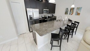 Une cuisine moderne avec des meubles de couleur sombre, des appareils en acier inoxydable, un comptoir en granit et un coin bar avec des chaises.