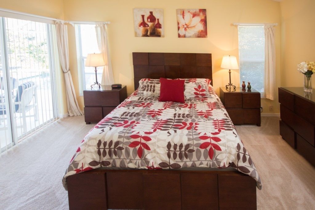 A bedroom with a large bed, two bedside tables with lamps, a nightstand, a window with curtains, and artwork on the wall.