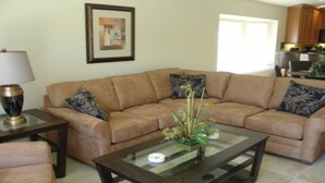 Ein Wohnzimmer mit braunem Sofa, zwei Beistelltischen und einem Glastisch mit Pflanze.