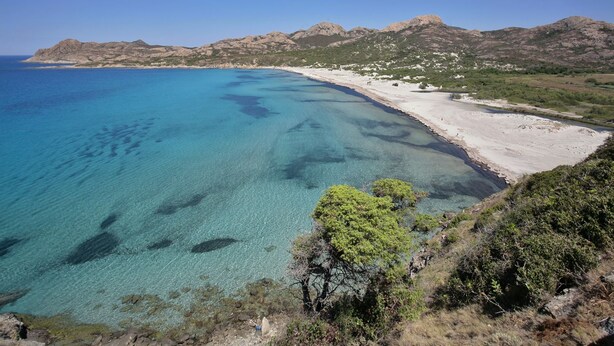 A coastal landscape with clear blue waters, a sandy beach, and rocky hills in the background. - Village Camping  de l'Ostriconi (Palasca)