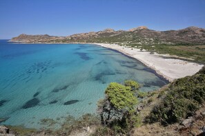 A coastal landscape with clear blue waters, a sandy beach, and rocky hills in the background. - Village Camping  de l'Ostriconi (Palasca)