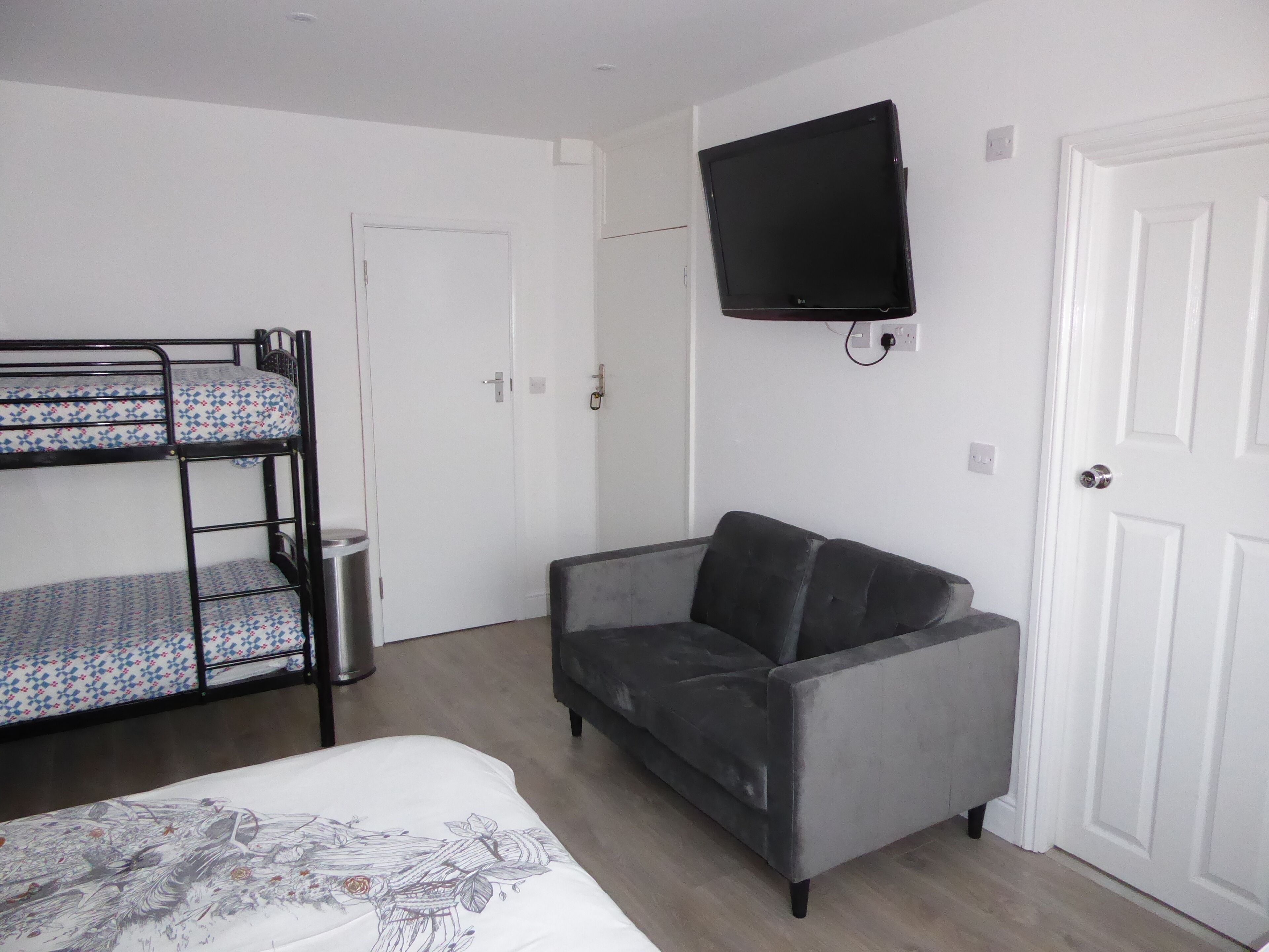 Una habitación con literas, un sofá gris, un televisor y una puerta blanca.