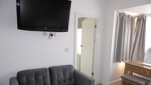 A room with a grey sofa, a wooden desk with a bench, a television mounted on the wall, and a door leading to another room. - Shenandoah House (Margate)