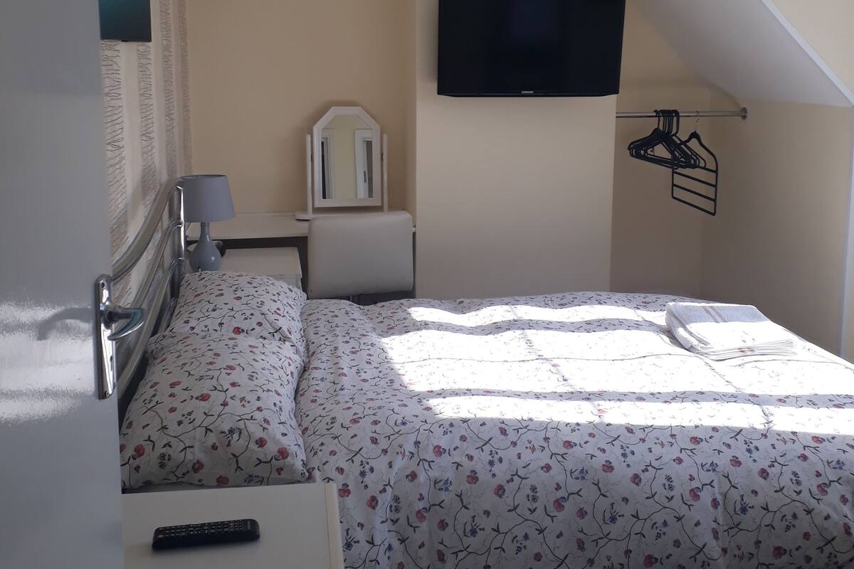 A bedroom with a bed, a bedside table, a lamp, a TV, and a mirror.