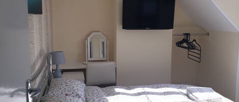 A bedroom with a bed, a bedside table, a lamp, a TV, and a mirror.
