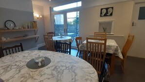 A dining area with a marble table, wooden chairs, a bookshelf, and a view through a glass door. - Shenandoah House (Margate)