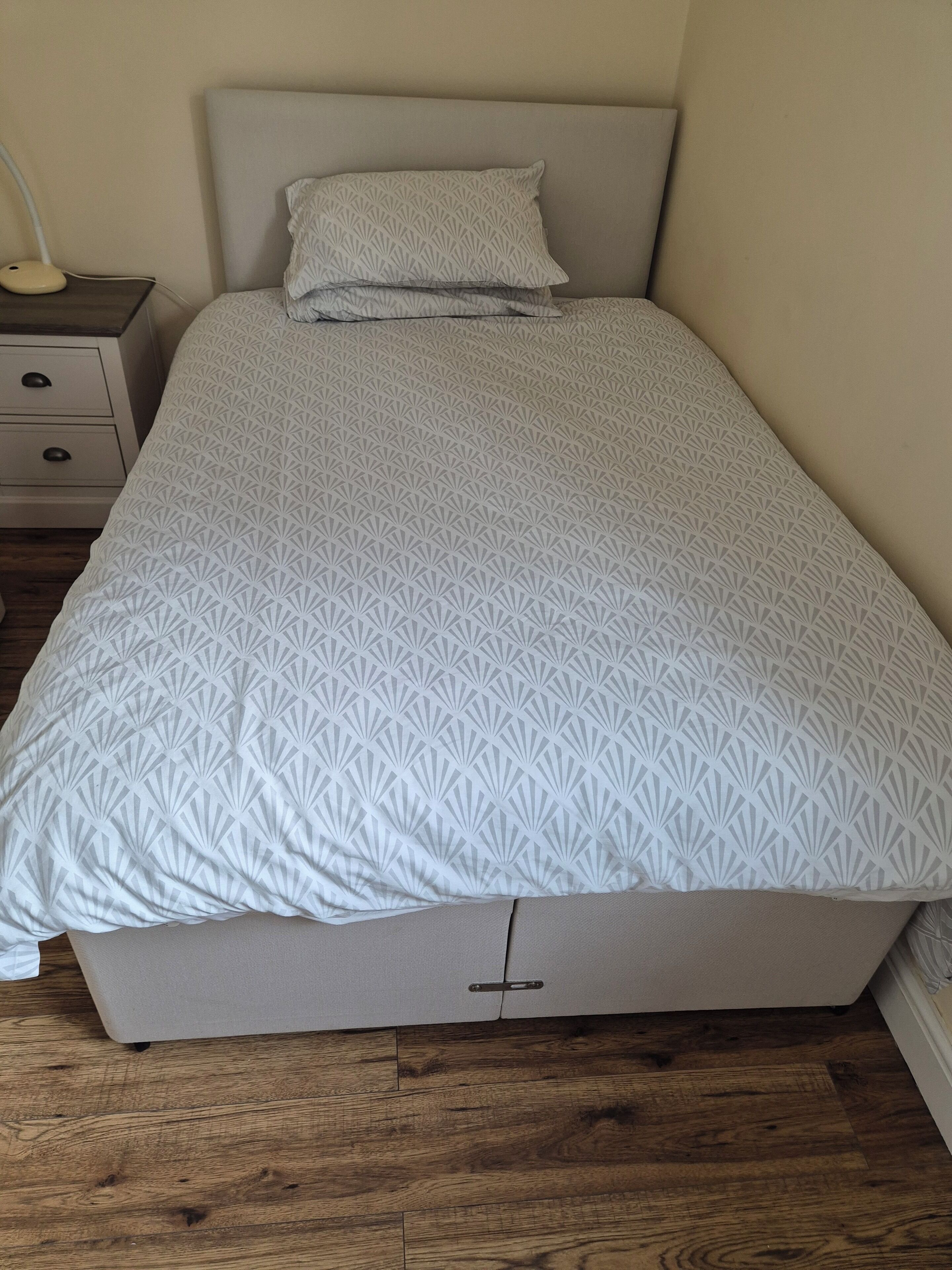 Una cama individual con una colcha de estampado geométrico, una mesita de noche con una lámpara y un aparador con cajones.