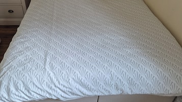Una cama individual con una colcha de estampado geométrico, una mesita de noche con una lámpara y un aparador con cajones.