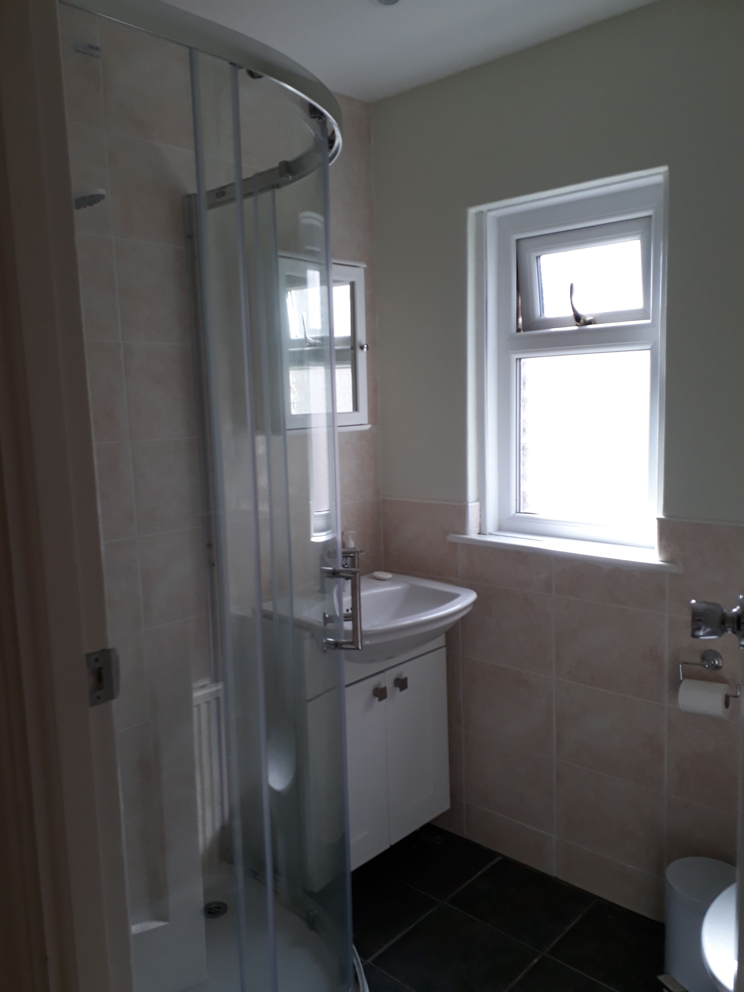 A bathroom with a glass shower enclosure, a sink, a toilet, and a window.