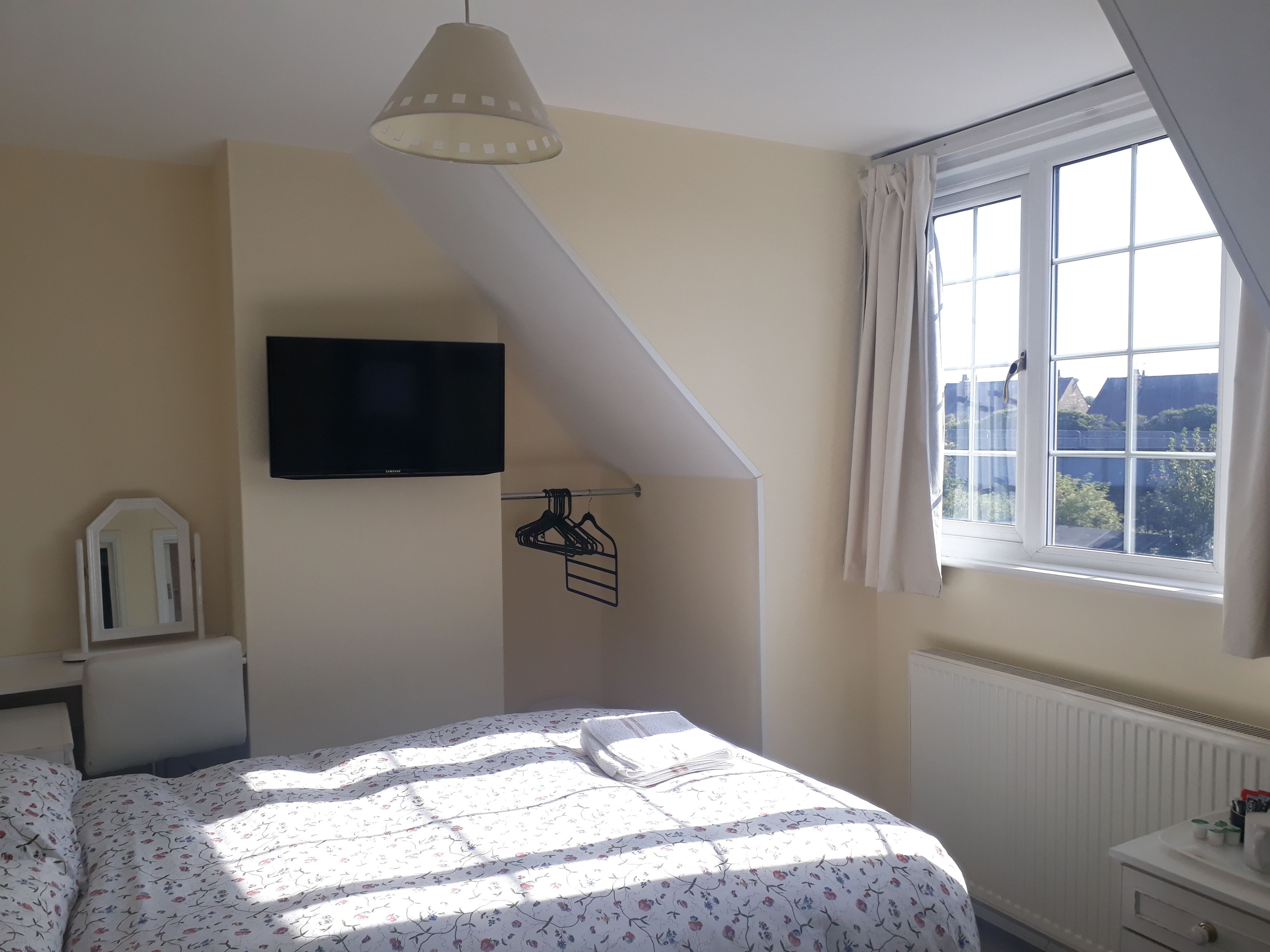 Une chambre à coucher avec un lit, un téléviseur fixé au mur, une fenêtre avec des rideaux et un radiateur.