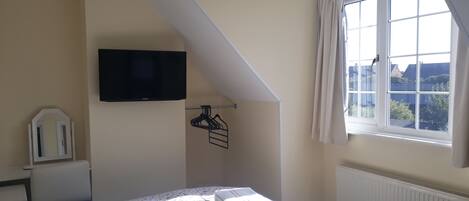 Une chambre à coucher avec un lit, un téléviseur fixé au mur, une fenêtre avec des rideaux et un radiateur.