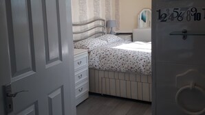 A bedroom with a bed, a dresser, a nightstand, a lamp, and a painting on the wall. - Shenandoah House (Margate)