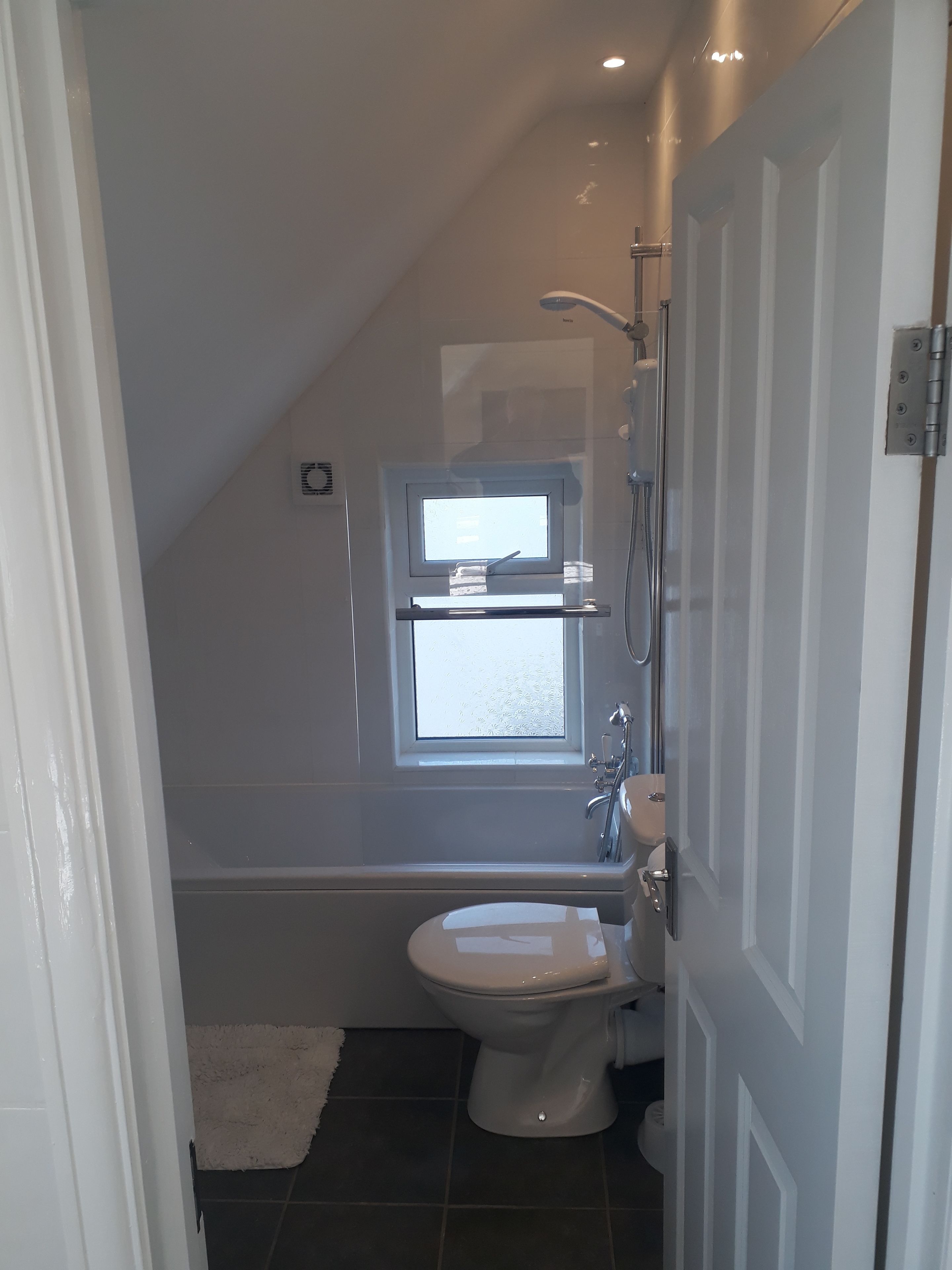 A small, modern bathroom with a toilet, a shower, and a window.