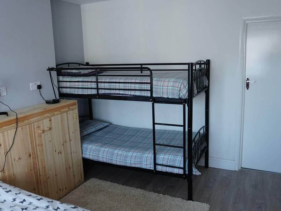 Una camera con letto a castello, un comò in legno e una scrivania con lampada.