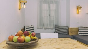 A room with a wooden table, a bowl of fruit, a sofa, and two wall-mounted light fixtures. - Astra Apartments (Naxos)