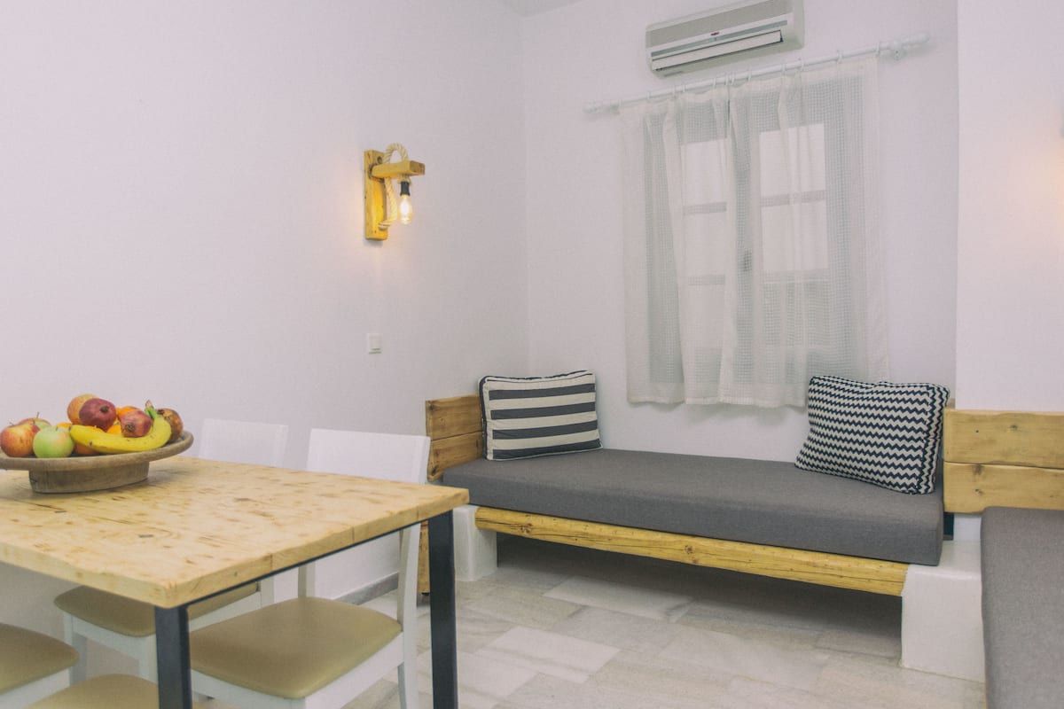 A small, cozy room with a wooden table, a bench with cushions, and a bowl of fruit on the table.