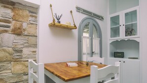 A room with a stone wall, a wooden table with chairs, a hanging shelf with candles, and a cabinet with glass doors. - Astra Apartments (Naxos)