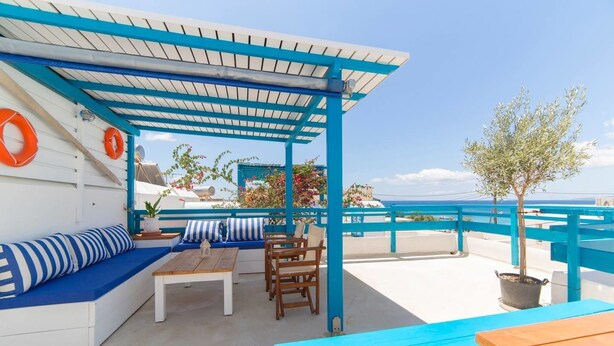 A rooftop terrace with a blue and white color scheme, featuring a seating area with a sofa and chairs, a table, and a potted plant. - Astra Apartments (Naxos)