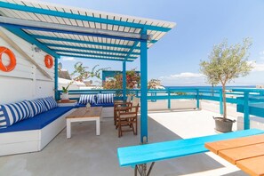 A rooftop terrace with a blue and white color scheme, featuring a seating area with a sofa and chairs, a table, and a potted plant.