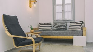 A cozy seating area with a wooden chair, a small table with a plant, and a cushioned bench with striped pillows. - Astra Apartments (Naxos)