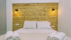 A bed with a wooden headboard, two white pillows, and two rolled towels on the bed. - Astra Apartments (Naxos)