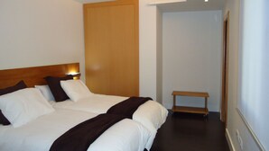 A hotel room with a large bed, a wooden headboard, a bedside table, and a small bench. - Apartamentos Turisticos Mauror (Granada)