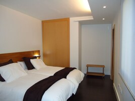Habitación de hotel con una cama grande, cabecera de madera, mesita de noche y un pequeño banco.