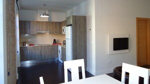 A modern kitchen with wooden cabinets, a microwave, and a refrigerator. There is a dining area with a table and chairs. - Apartamentos Turisticos Mauror (Granada)