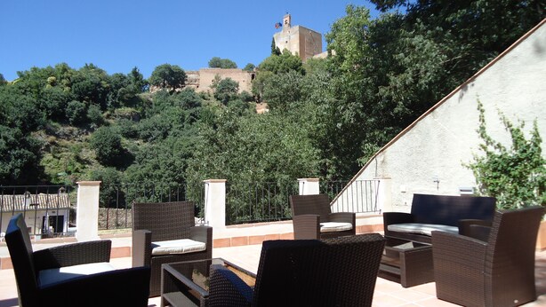 An outdoor seating area with wicker furniture and a view of a hill with a building. - Apartamentos Turisticos Mauror (Granada)