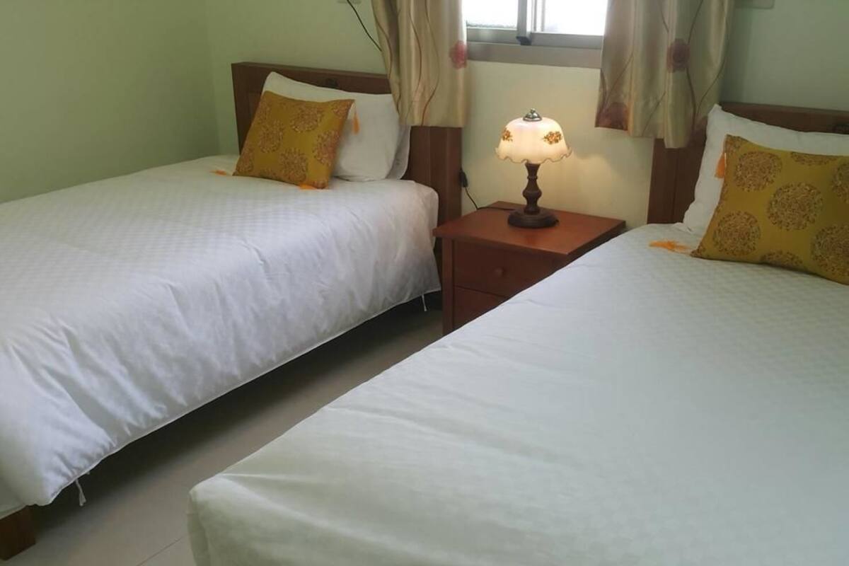 A hotel room with two single beds, each with a pillow and a nightstand with a lamp.
