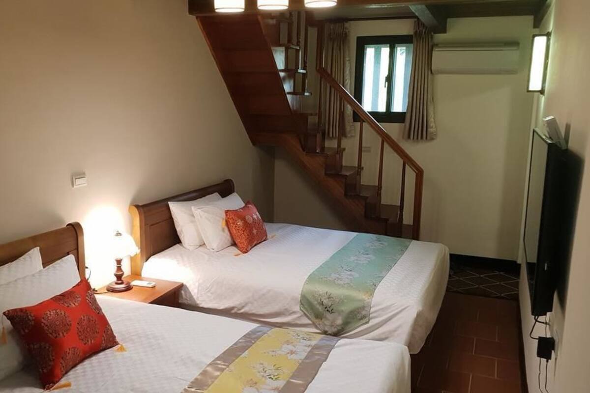 A hotel room with two beds, a wooden staircase, and a television on the wall.