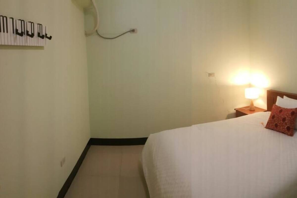 A hotel room with a bed, a nightstand, a wall-mounted lamp, and a wall decoration.