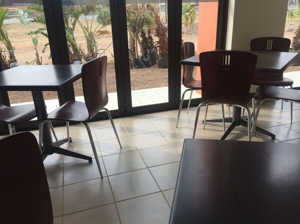 Un restaurante con asientos dentro, ventanas amplias y plantas en macetas.