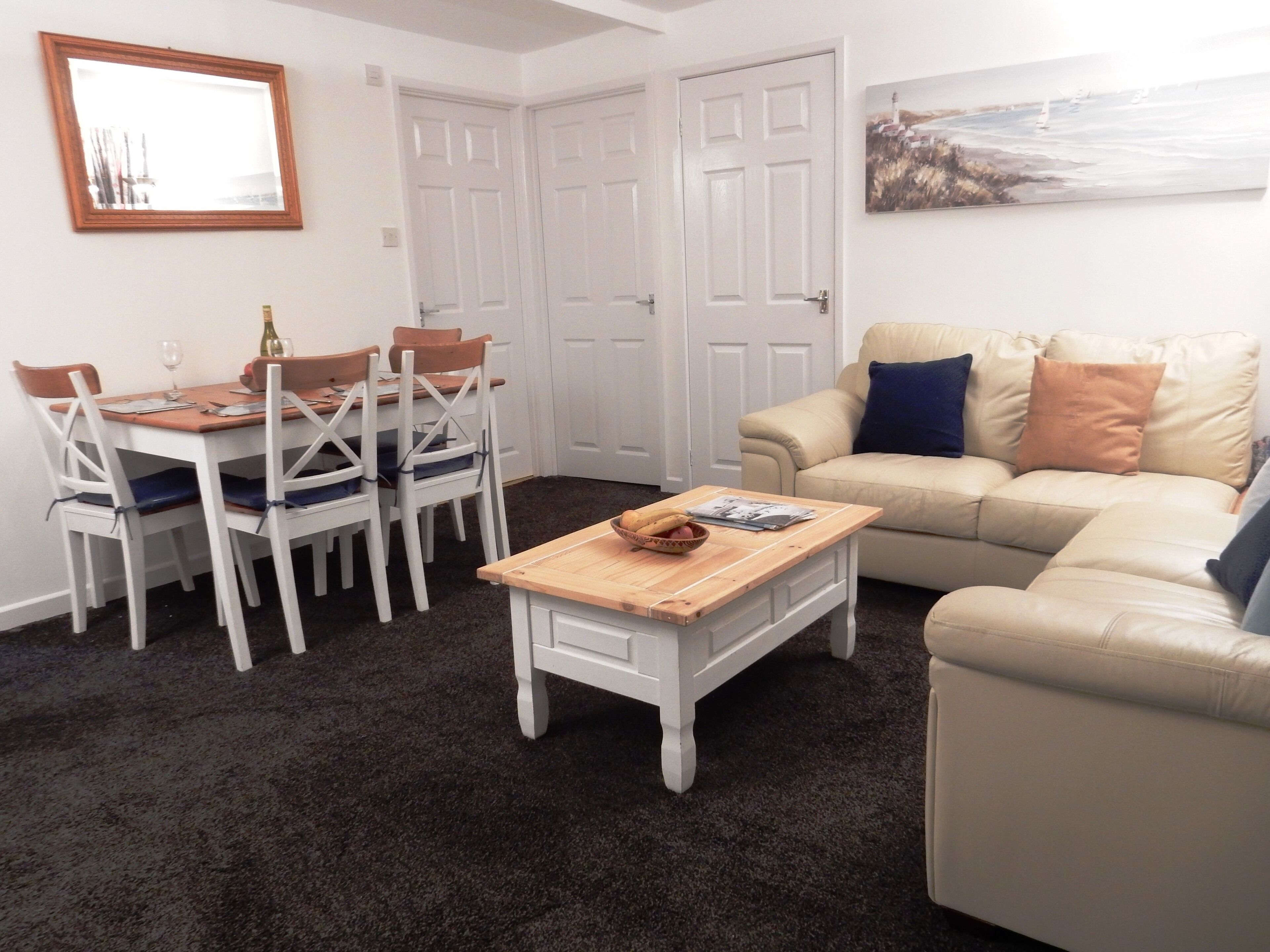 Una sala de estar con comedor, un sofá color beige, una mesa de centro de madera y puertas blancas.
