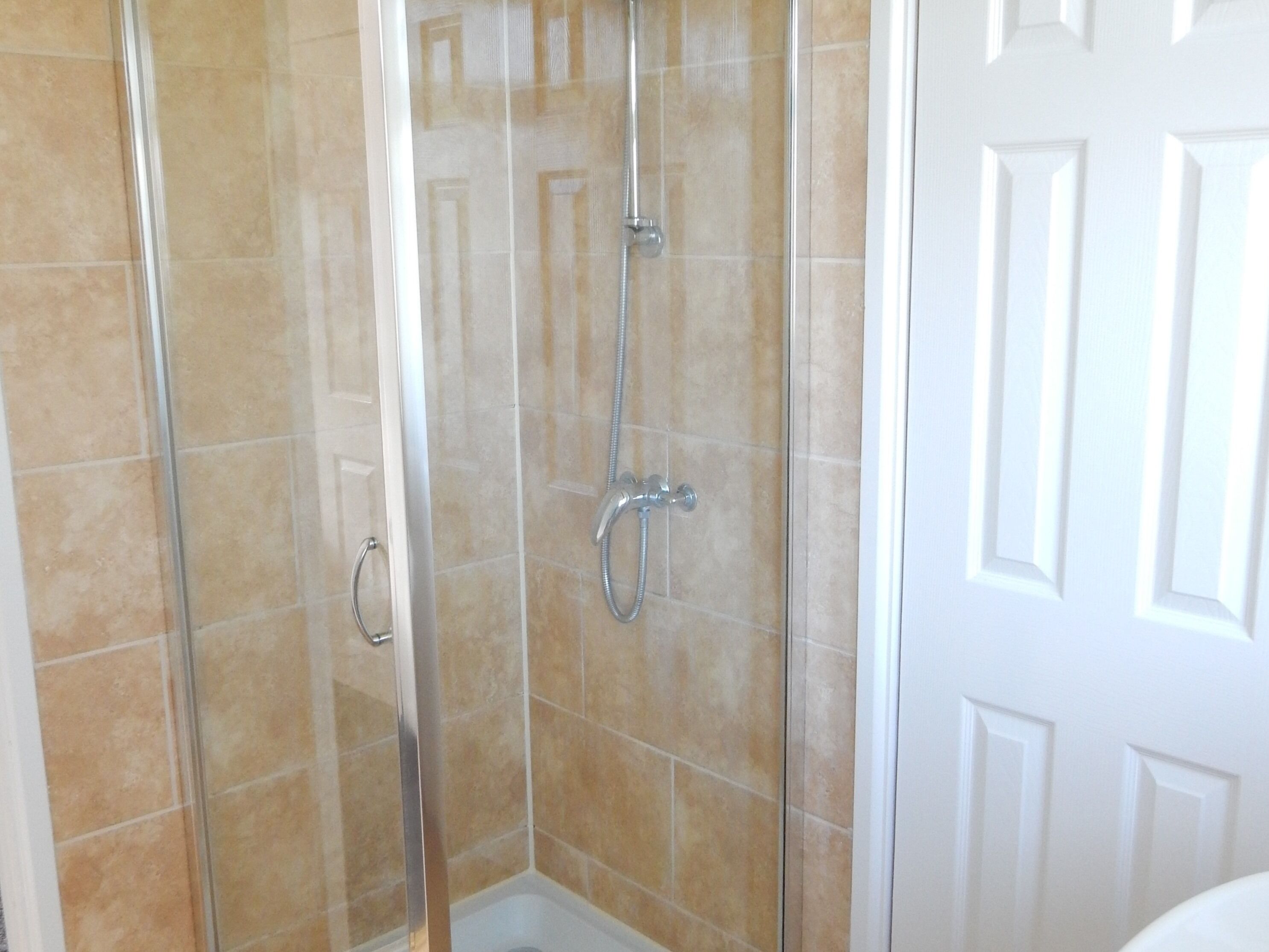 A glass-enclosed shower area with a white door and beige tiles.