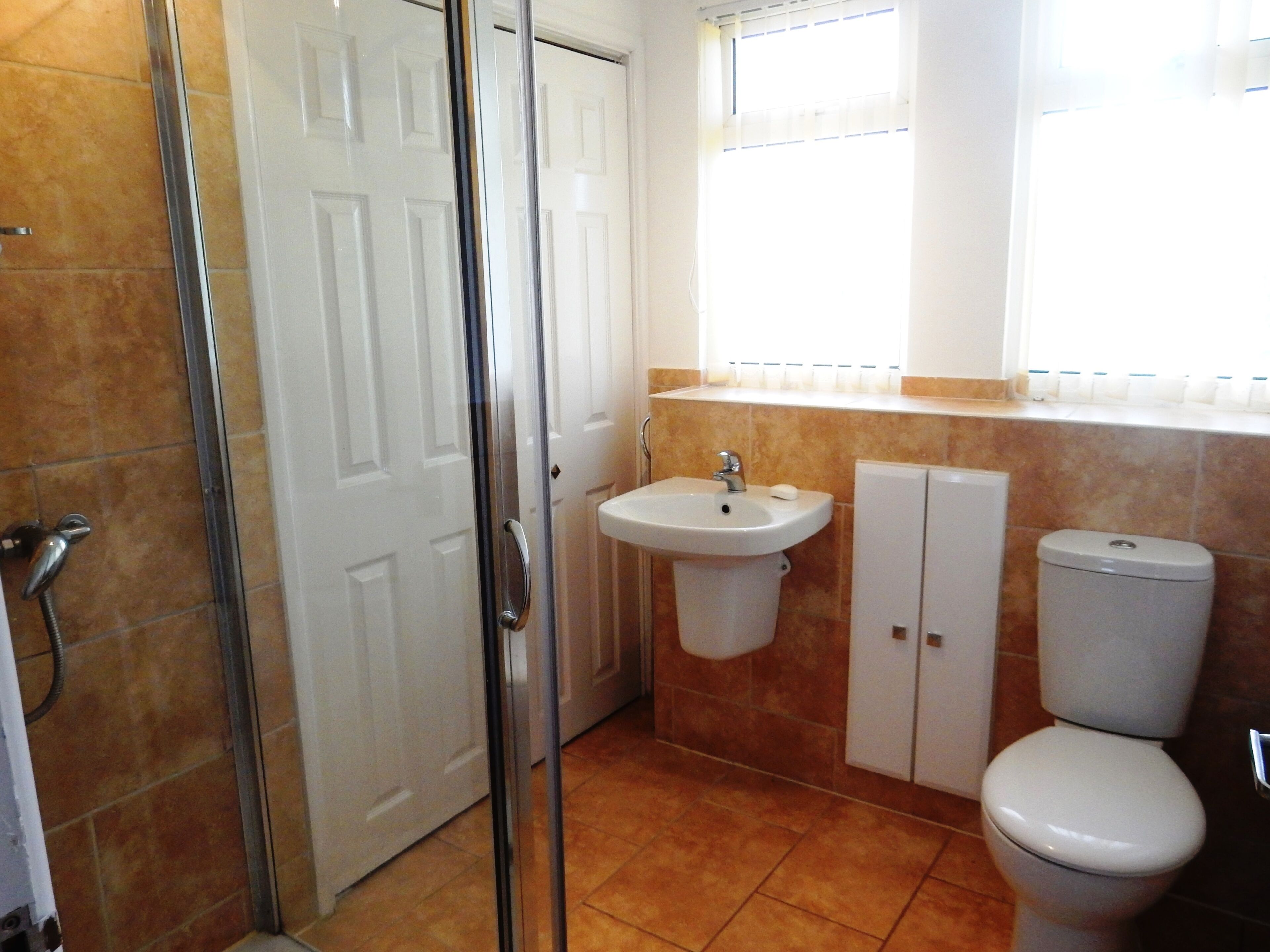 Une salle de bain équipée d’une douche, d’un lavabo, de toilettes et d’une fenêtre avec des stores.