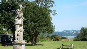 A statue in a grassy area with a bench and a view of hills and water in the background. - Dartmouth Chalet Holidays (Dartmouth)