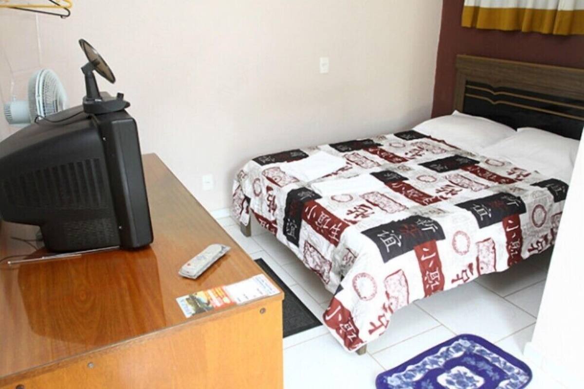 Une chambre d’hôtel avec un bureau en bois, un lit recouvert d’une courtepointe à motifs et un petit tapis bleu sur le sol.