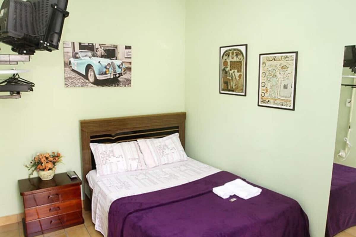 Une chambre à coucher avec un lit, une table de chevet, une commode et deux tableaux encadrés accrochés au mur.
