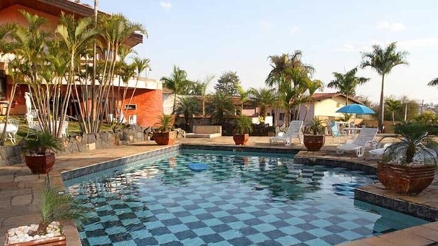 A swimming pool with a checkered pattern, surrounded by lounge chairs and potted plants. - Pousada Sorocaba (Sorocaba)