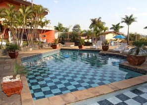 A swimming pool with a checkered pattern, surrounded by lounge chairs and potted plants. - Pousada Sorocaba (Sorocaba)