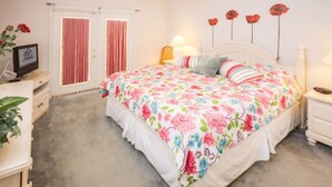 A bedroom with a floral bedspread, a bedside table with a lamp, a dresser, and a door with curtains. - Ip60497 - Island Club West - 3 Bed 2 Baths Condo (Kissimmee)